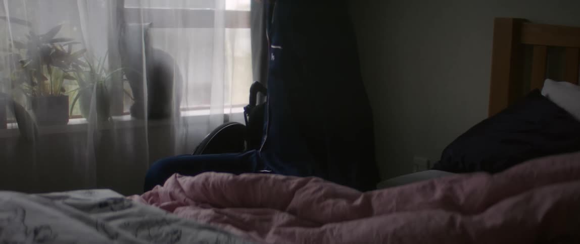 Woman with brown hair and dark blue pajamas gets out of bed and sits in wheelchair