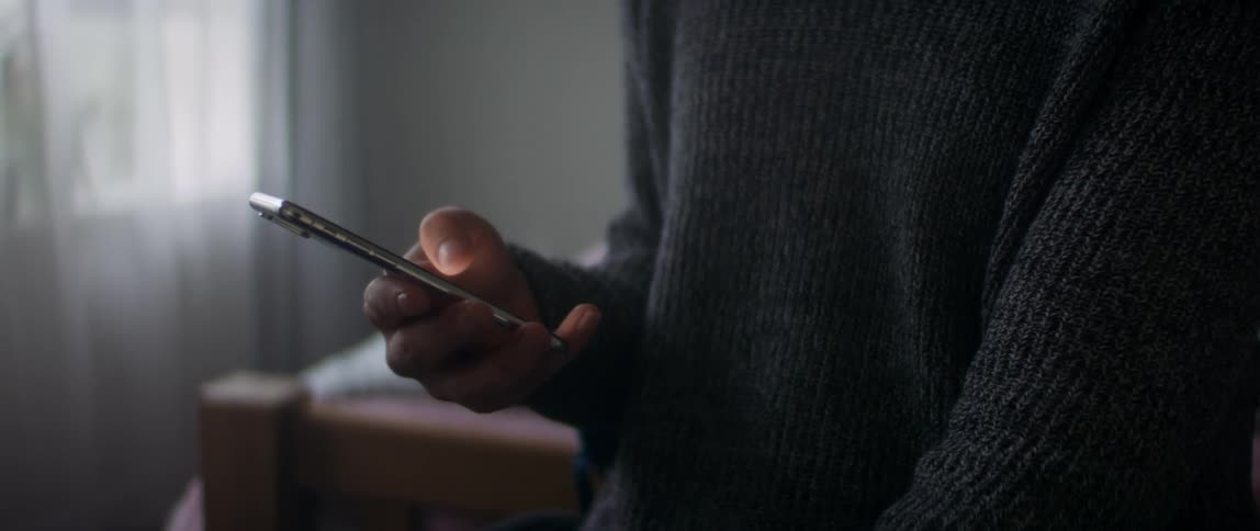 A man scrolling on a smartphone while standing in a bedroom