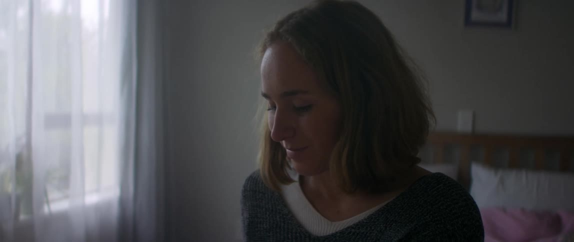 A woman sits in her bedroom at home and smiles