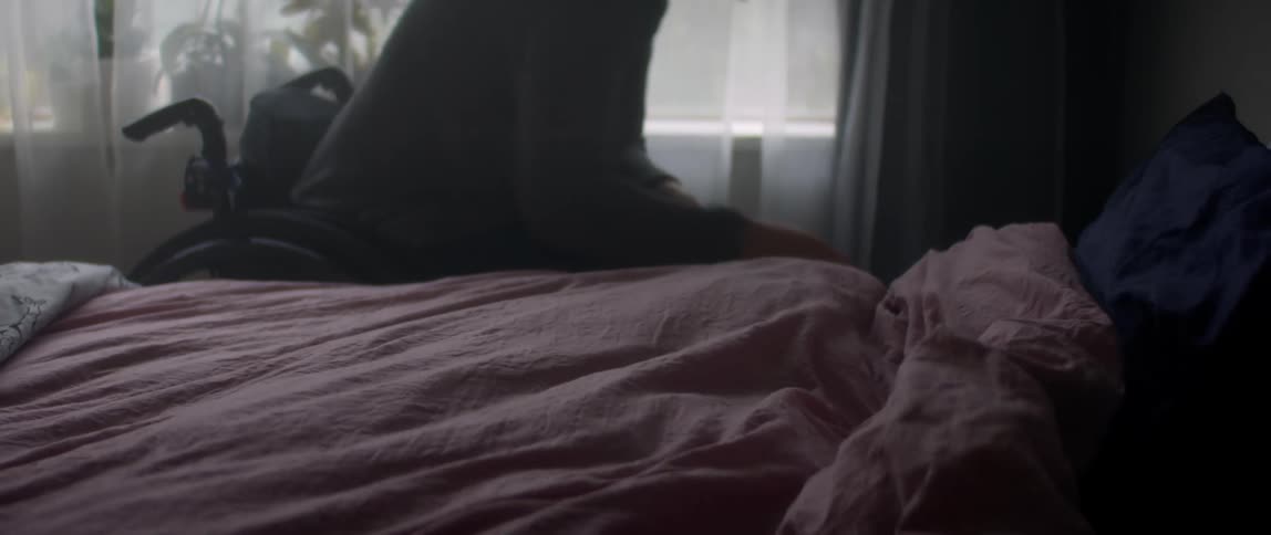Woman in wheelchair makes bed in bedroom