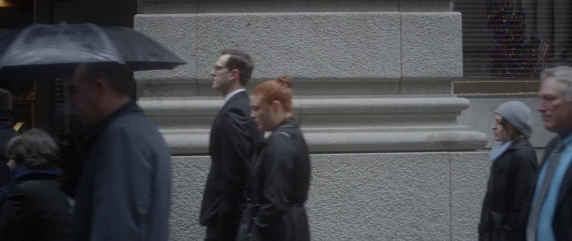 Pedestrians walk along a city sidewalk with umbrellas on a rainy day