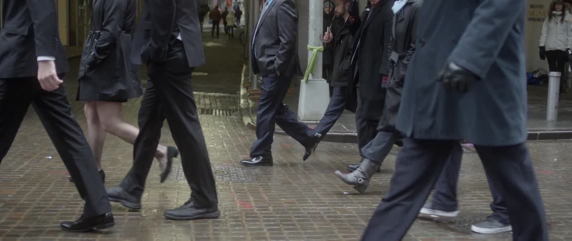 A crowd of people walking along a brick-paved street on a rainy day