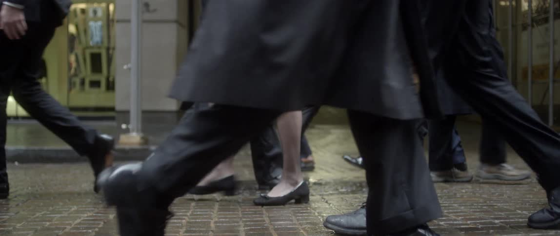 People walking along a wet, brick-paved street in front of shops