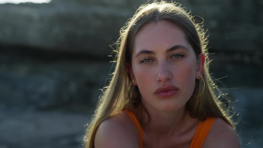 Model wearing makeup poses near rock formation on sunny day