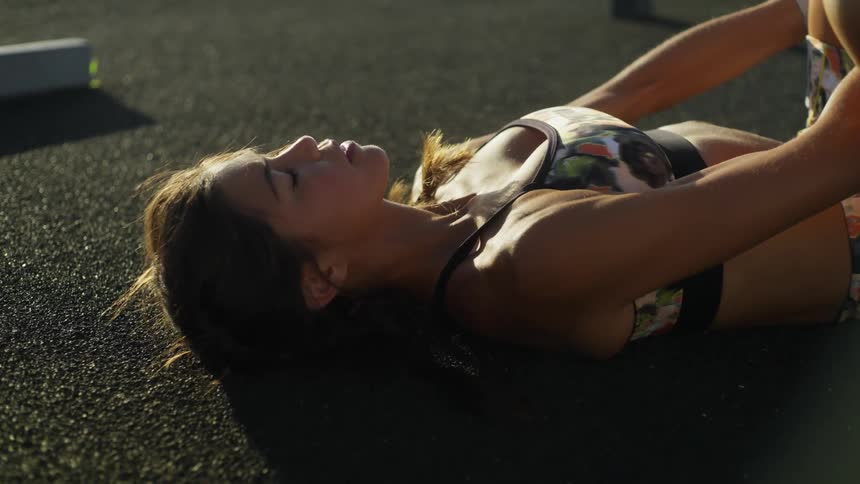Sunlight shines on a teenage girl as she lies down on the ground holding her leg in the air