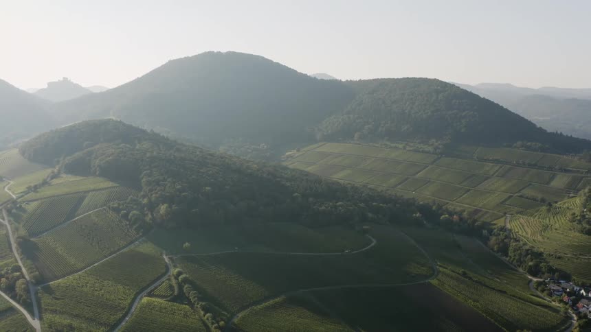 Fog covers mountains and crop fields near town as vehicle moves along road on slope