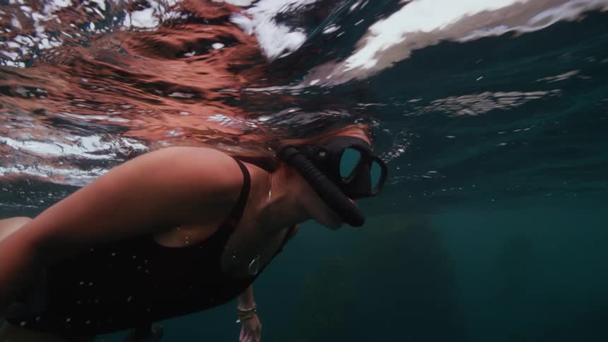 A woman is swimming just below the water surface wearing a mask and snorkel