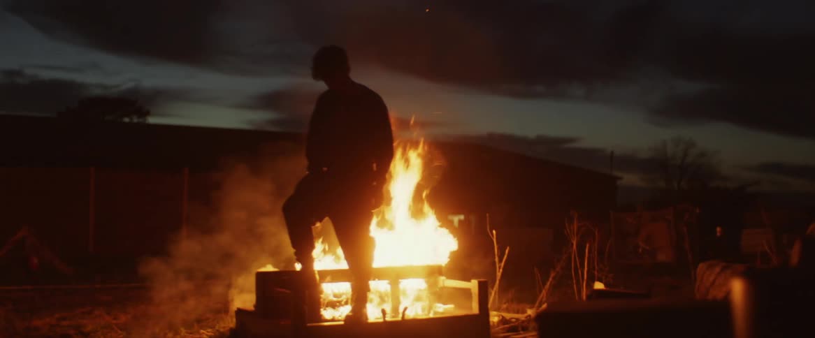 Man is silhouetted agains the bonfire in the field at dusk
