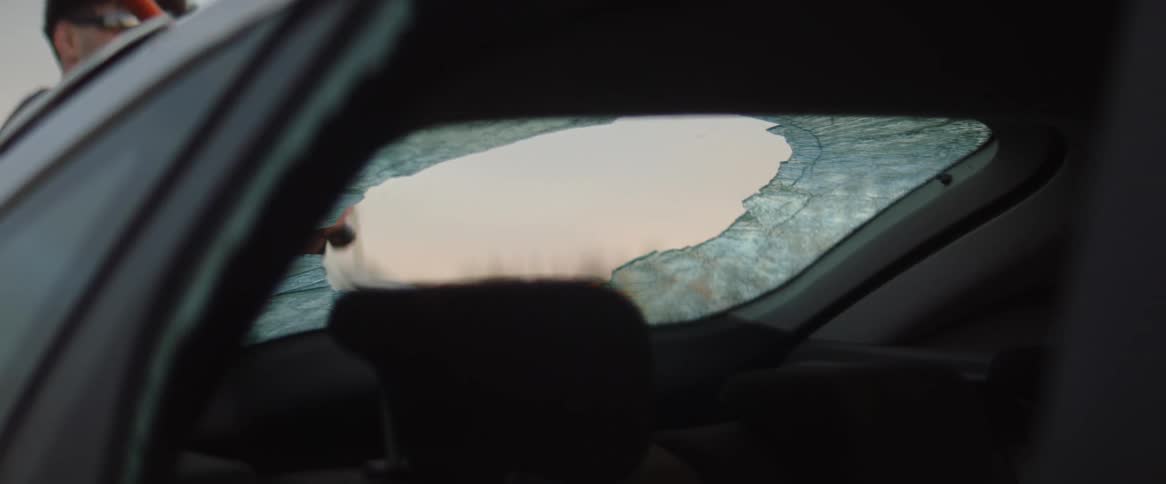 Man with sunglasses and black hat hits car with sledgehammer