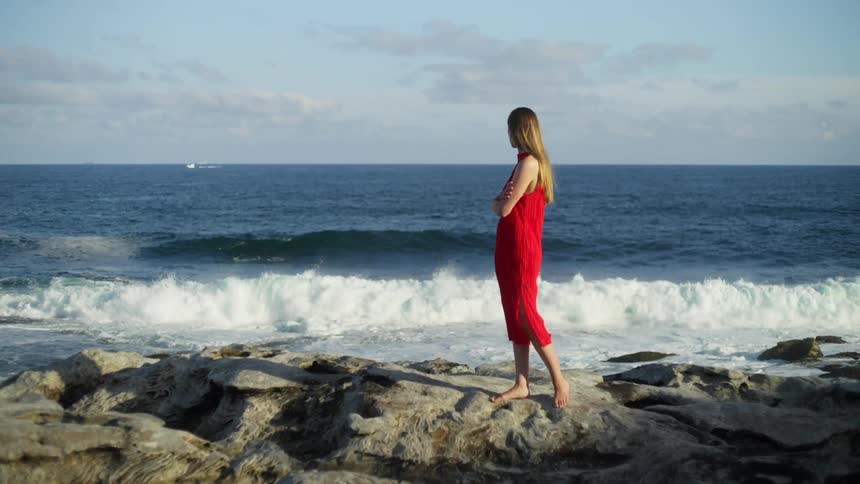 Waves crash towards the shore where a woman stands with her arms crossed
