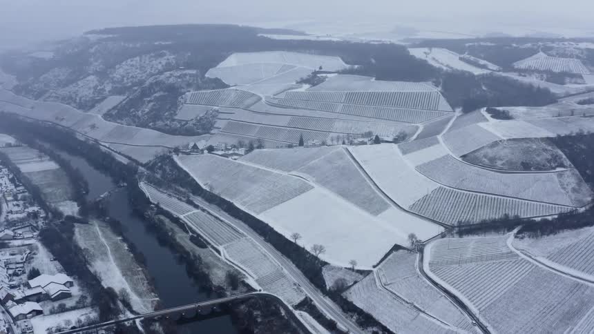 Bridge crosses river connecting crop fields and town in winter
