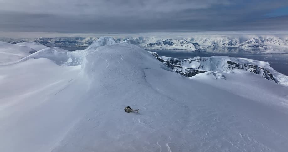 The rotor of a helicopter is spinning as it sits on a snow covered mountain