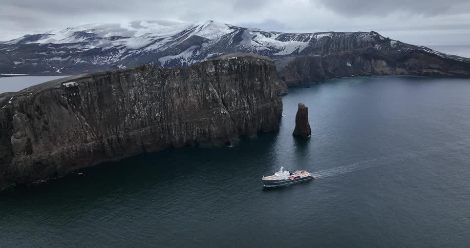 A yacht travels past snow capped mountains in Antarctica