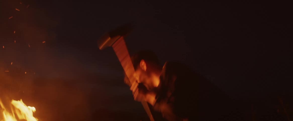 A boy swinging a sledge hammer at a bench in a bonfire