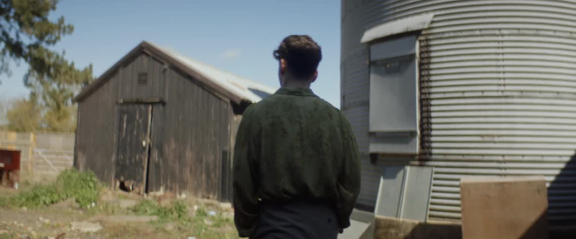 A young man walks through a barn toward a silo on an abandoned farm