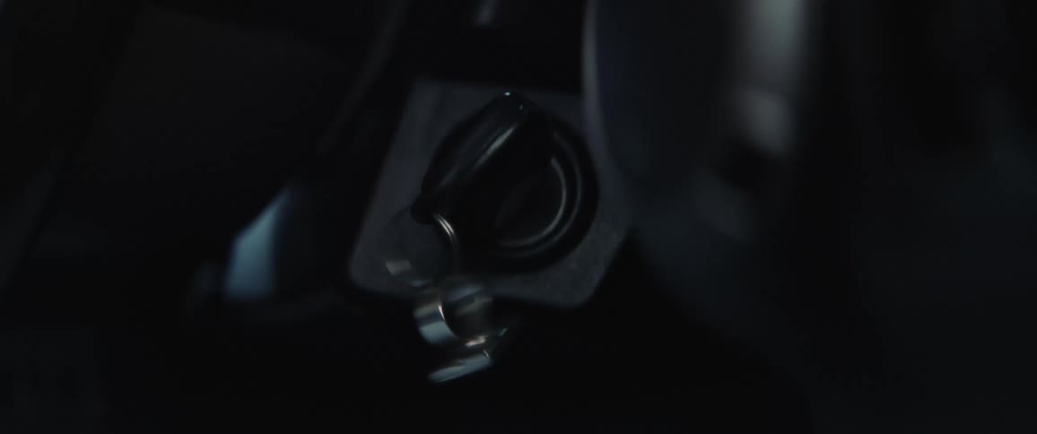 A hand is on the ignition key of an automobile and they turn it to start the engine