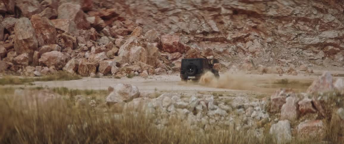 A black jeep drifting and spinning up dirt on a sandy road near a rocky mountain