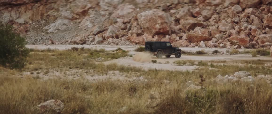 A black jeep is turning around near a boulder on a desert mountain dirt road