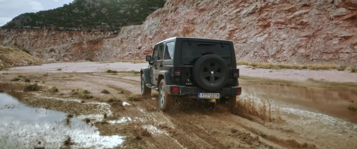 Black jeep drives through puddle in the field