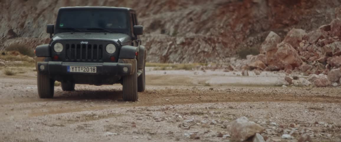A man drives his jeep down a gravel path below a canyon