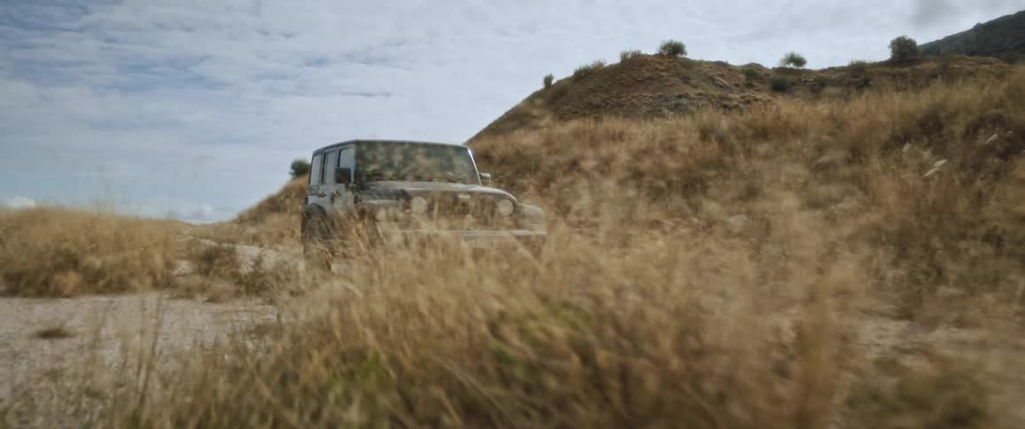 A jeep drives off road past hills