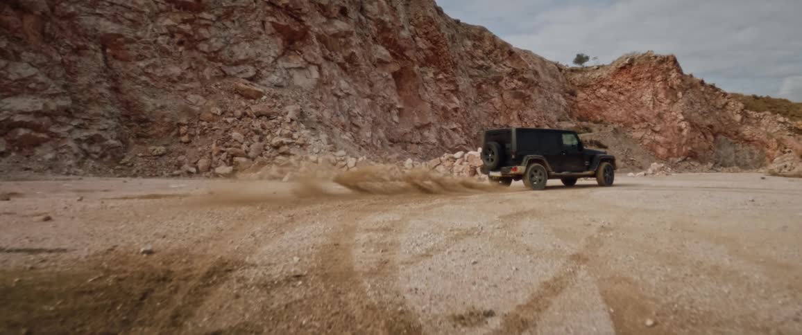 Black jeep drifts to the right in the field near mountain