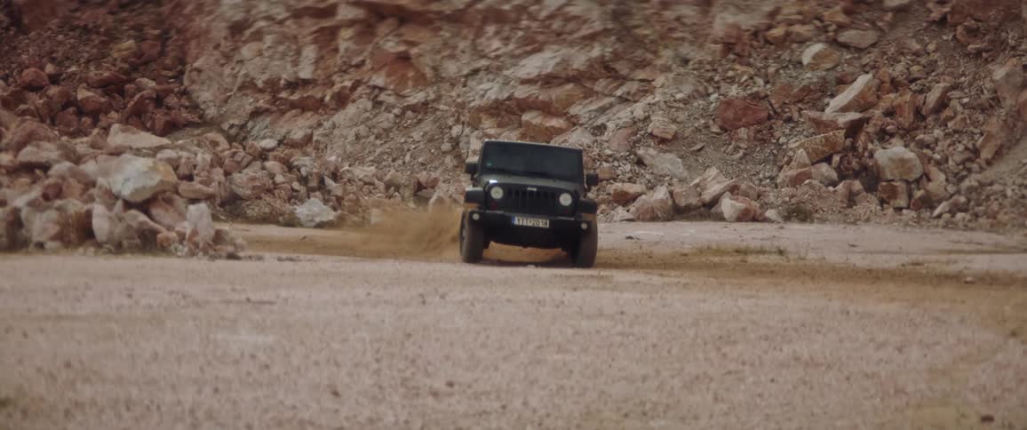Black jeep drives in field near mountain
