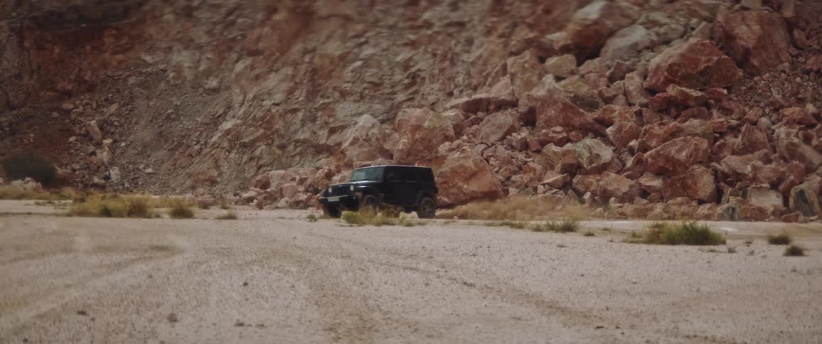A sport utility vehicle drives out from in front of a huge mountain of rocks skidding on the dirt and driving forward