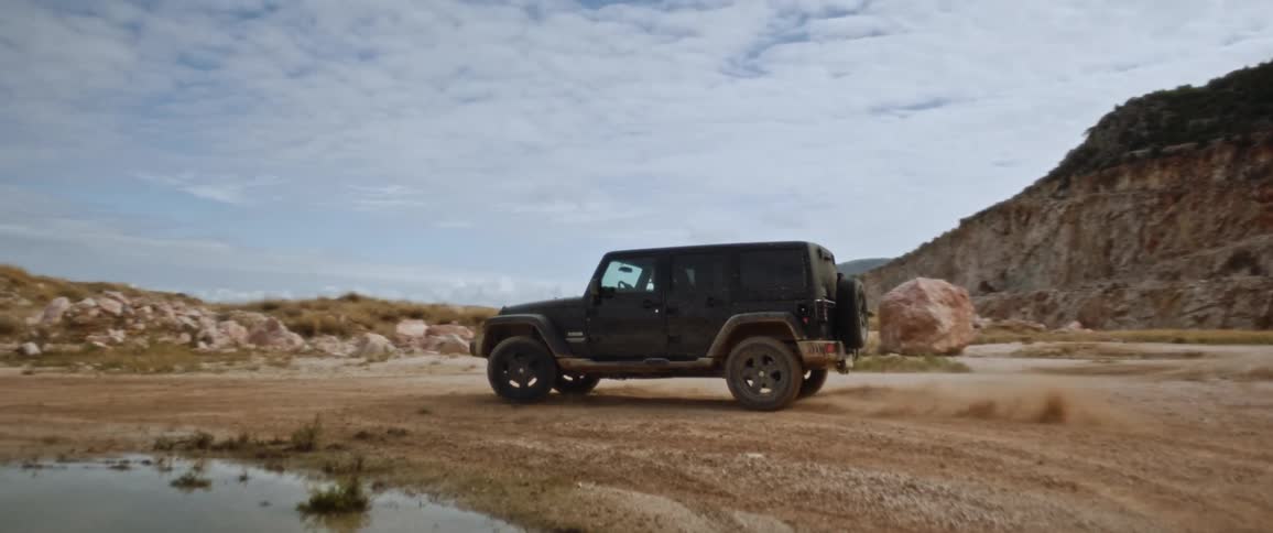 Sport utility vehicles drives around kicking sand on a deserted area next to a mountain