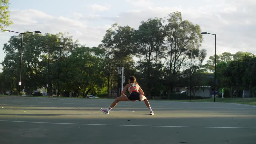 A teenage girl is in an open court either stretching or getting ready to run