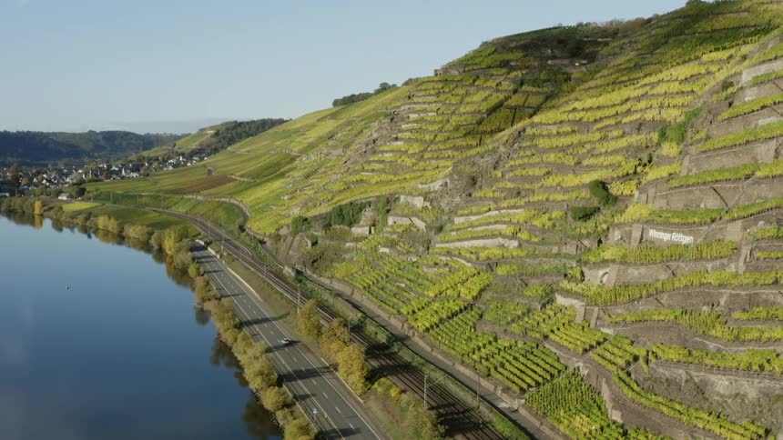 Automobiles travel on a road along the river in the valley and vineyards line the mountain hillside