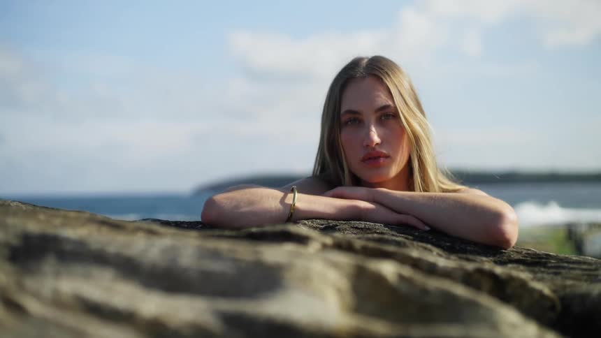 Woman turns her head and looks forward while crossing her hands under her chin leaning on a rocky ledge