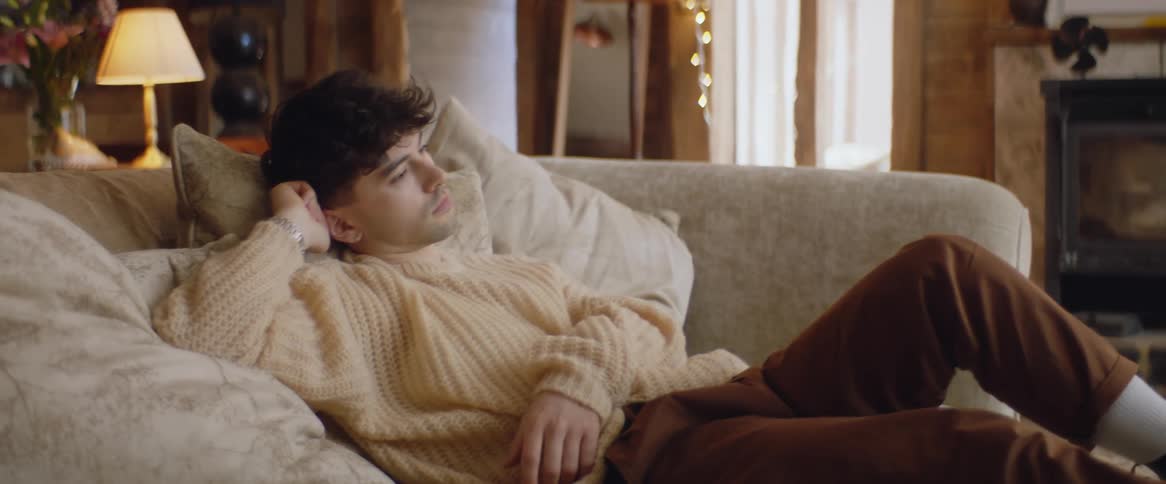 Man wearing sweater reclines in living room while watching