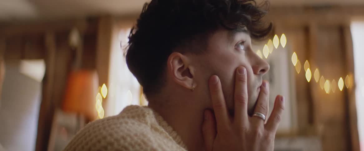 A sad looking teenage boy at homes rests his face in his hands and then runs his hands through his hair