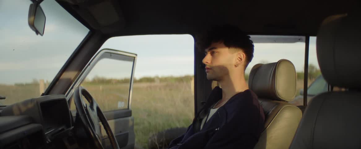 Man sits on driver seat of right hand drive car with the door open to a field