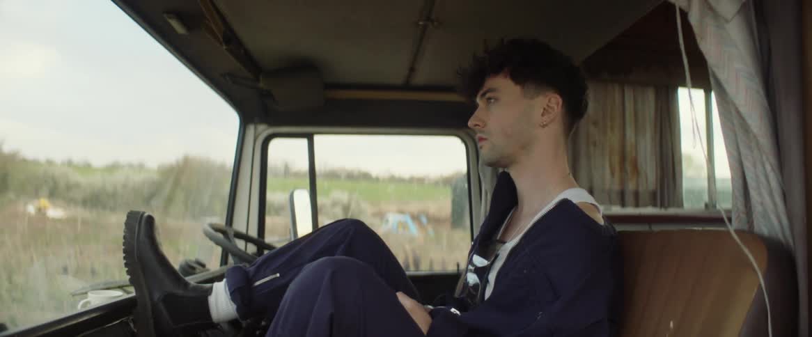 A teenage boy sits in a vehicle with his foot on the dashboard