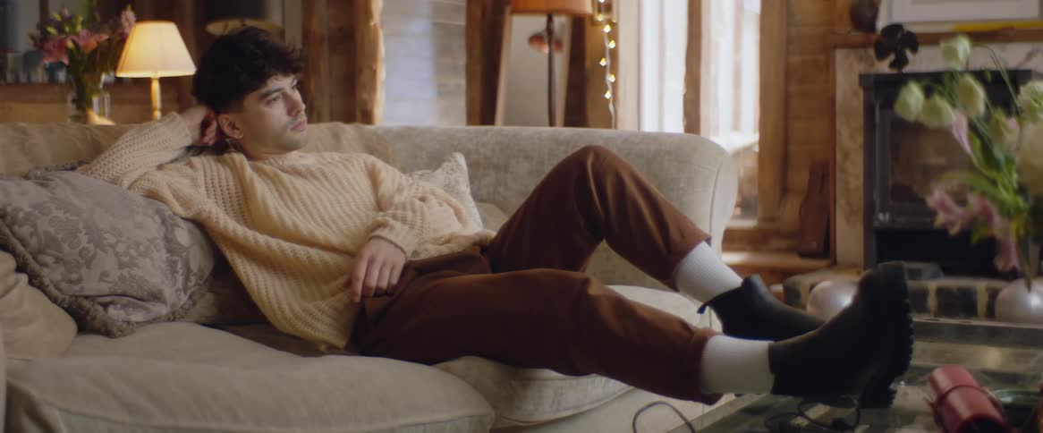 A teenage boy is sitting back on the couch with his feet on the living room table