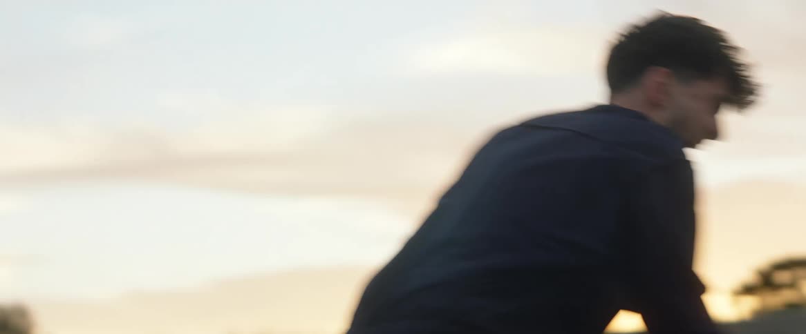 Angry man with black jacket swings sledgehammer at sunset