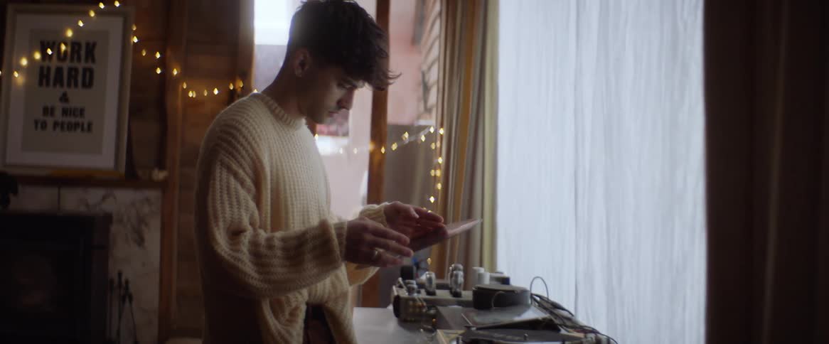 A man in a yellow sweater picking up a record disc and looking at it contemplatively