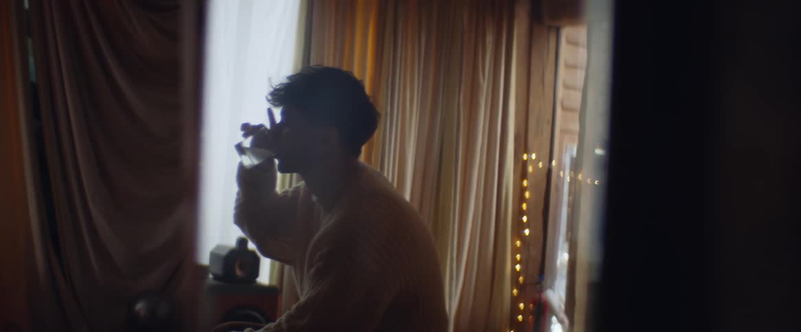 Teenage boy sitting in a room drinking alcohol middle of day