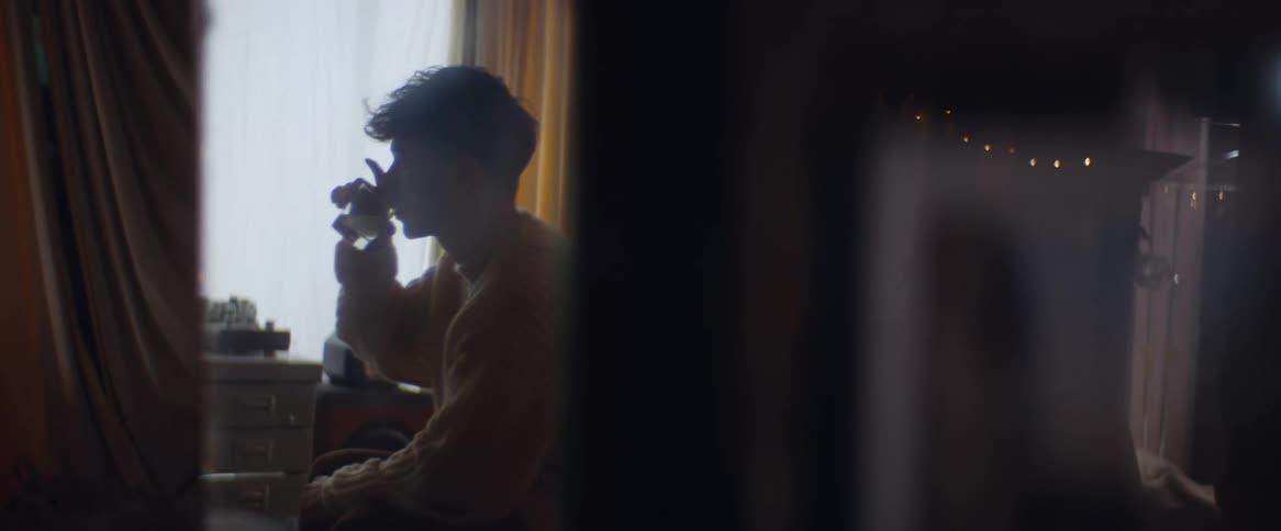 A male in a yellow sweater sitting drinking out of a shot glass