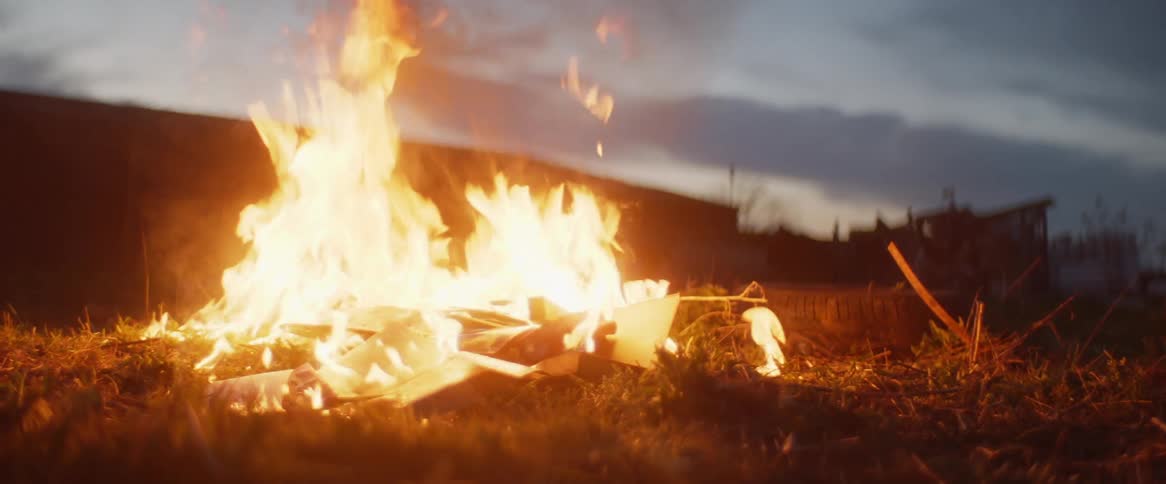A person drops a match onto debris to start a fire in a field