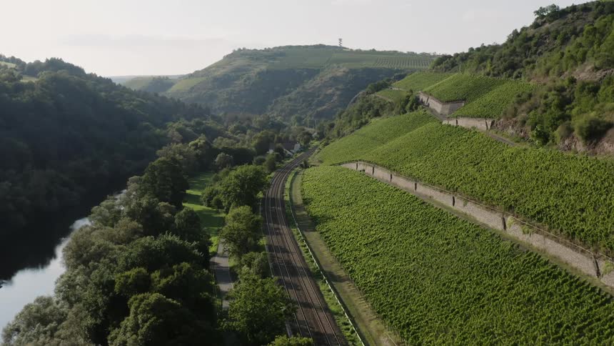 Aerial of river and train tracks alongside a mountainside in the country