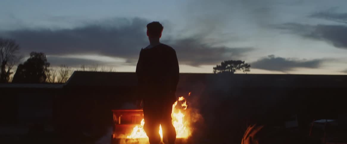 A man is outside standing in front of a piano that is on fire