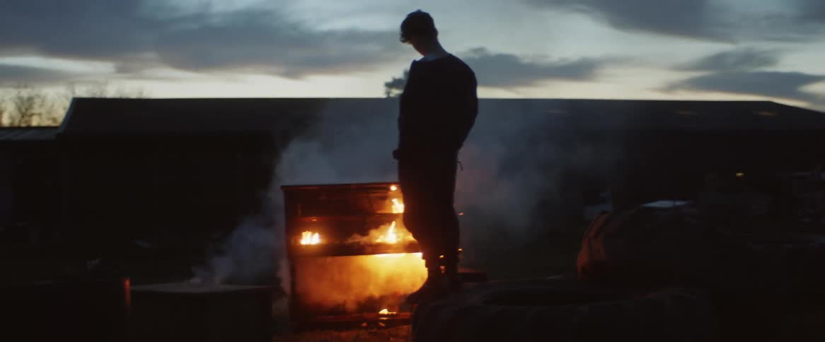 Person stands outdoors next to a burning piano