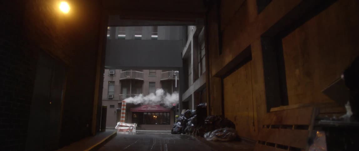 A dark alley leads to tall buildings ahead