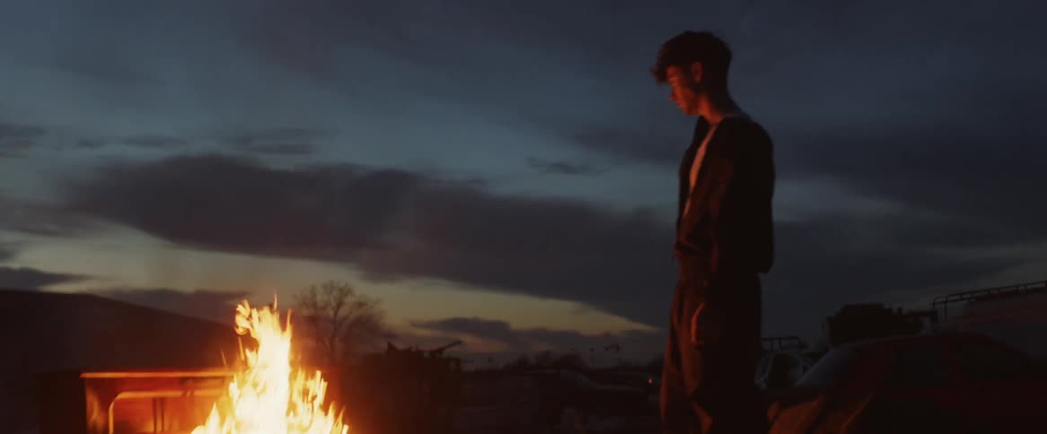 A man standing in front of a bonfire at dusk