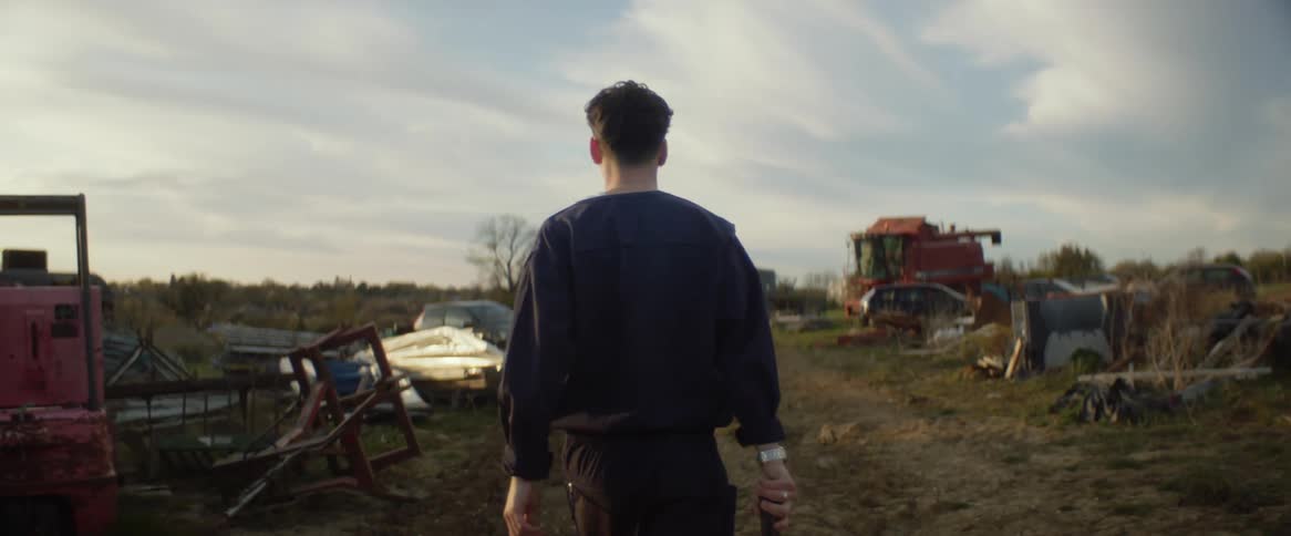 A man walking among piled up junk holding something in his right hand
