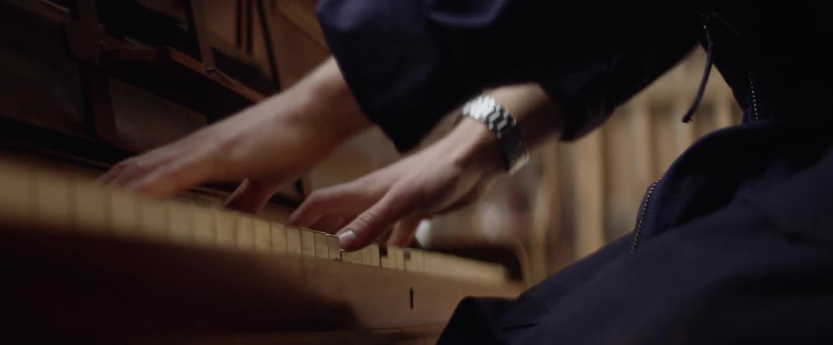 A young man stands up while playing the piano in a barn