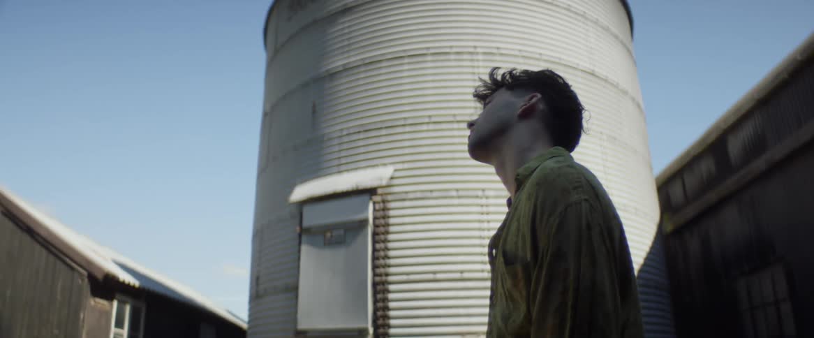 Man looks up while standing outdoors near a corrugated metal silo
